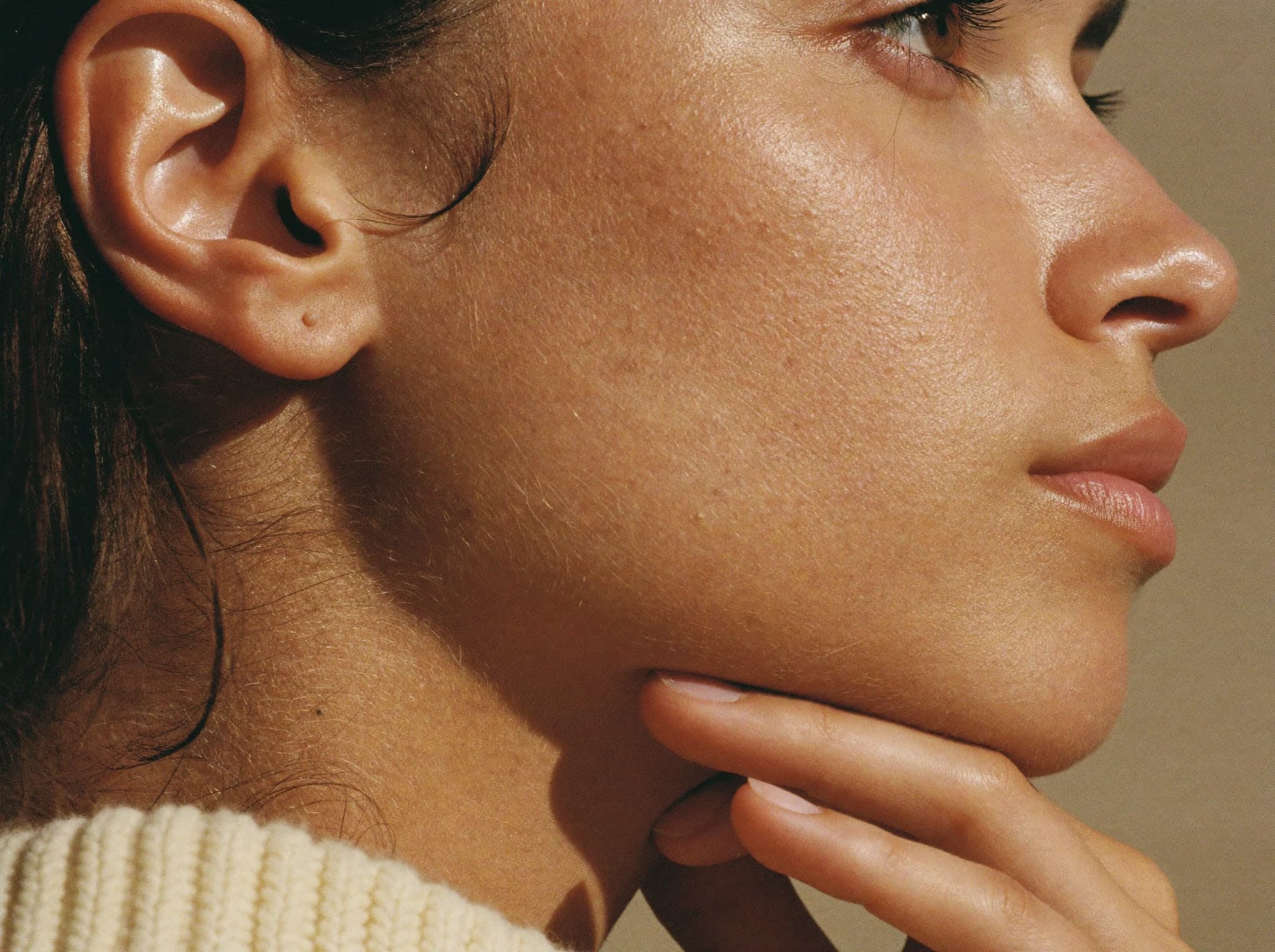 Close-up of a woman’s profile in warm light, fingertips resting under her jaw